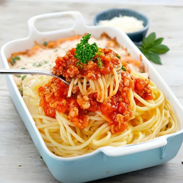 Spaghetti with meat sauce and parsley on a fork, served in a light blue baking dish.