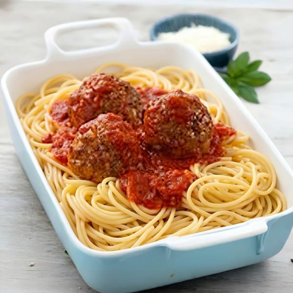Spaghetti and meatballs in a light blue baking dish with a side of grated cheese and basil.